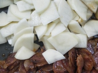 12、酱香土豆炒腊肠,把腊肠拨到锅边一点，倒入沥干水的土豆片。