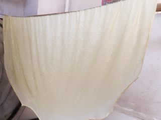 13、纯手工豆腐皮,如图：用双手将龙须拉起，一张白色的豆腐皮就从锅中捞起来了。
