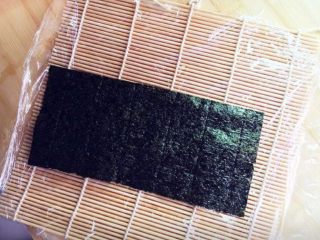 5、樱花寿司,首先将寿司帘上铺上保鲜膜，再放上一片海苔。