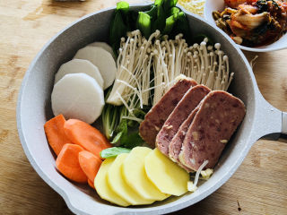 6、部队火锅,把准备好的蔬菜码到平底不粘锅中，我这里的食材有白萝卜、胡萝卜、土豆、午餐肉、金针菇、生菜、辣白菜。