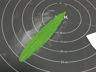 10、粽子表情包馒头,从绿色面团中分隔一点小面图出来，搓成椭圆形，硅胶垫上撒粉防粘，用擀面杖擀长。用刮板压出条纹，成粽叶的纹路。