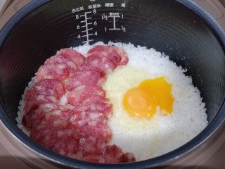 12、懒人煲仔饭--电饭煲版,再把切好的阿赐酱腊肠摆放在米饭上面，将鸡蛋磕米饭上！盖上盖子继续煮饭模式5分钟，这时电饭煲掉到保温，不要急着打开盖子，焖15分钟！