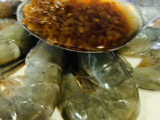 16、蒜蓉蒸大虾,用勺子,把炒好的蒜蓉浇在每只虾上;