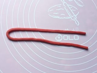 11、五福灯笼,另取红色面团擀开，用小刀切割出一条长25cm、宽0.3cm的长条。