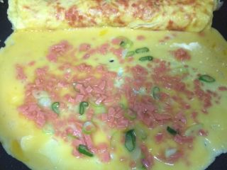 12、火腿葱花厚蛋烧,把卷好的第一层放在锅边，剩下的鸡蛋液倒入锅中，继续重复第一层的步骤，转动锅成圆形受热均匀