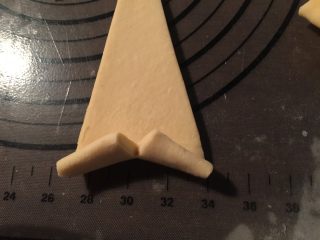 11、流沙起酥包,取一个小三角形面片，在三角形底部中点处划一道口子；用两只手，捏住两个角，向上卷在顶部的小尖上刷一层全蛋液