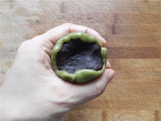 11、青汁月饼,饼皮包住豆沙馅，用虎口慢慢把饼皮往上推（尽量做到让月饼皮均匀覆盖在馅外面。不均匀的地方可适当推补一下，保证完美），收好口。