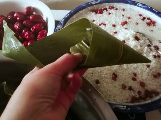 5、红豆粽子,取一片粽叶，剪掉根部，挽成三角漏斗形状。