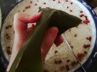 9、红豆粽子,用粽叶向下盖住漏斗顶部交汇处 用手捏出一个角。