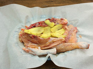 2、珐琅锅盐焗鸡,鸡肉两面均匀抹上盐焗鸡粉，摊开油纸，放入鸡肉，将姜片铺在鸡肉上面