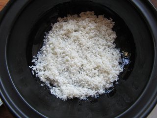 6、腊肉煲仔饭,将洗好的大米均匀铺在锅底