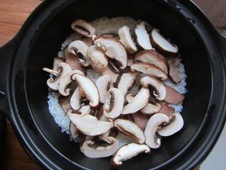 9、腊肉煲仔饭,蜂鸣声响起时把香菇、口蘑片铺在表面，在锅四周淋入一勺食用油，加盖再次启动按钮