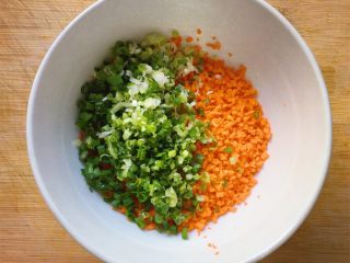 4、香煎米饼~,将切好的红萝卜末放入大碗中,加入葱花