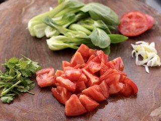 2、冬至美食~番茄青菜牛肉面,番茄洗净后用刀切成滚刀块,香菜切段,葱切碎,青菜切开。