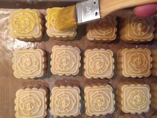 51、自制奶黄馅广式小月饼,取出烤盘,月饼放至40度以下,开始刷蛋黄液,刷两遍,留少许蛋清是为了防止蛋黄液太浓稠,加两滴水也可以,但千万不要多了