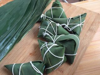 3、红豆粽子,取一张叶子，一前一后卷成锥形，填好主材(因只有我一个人，手是湿的无法拍照，请理解)，按照自己的想法卷成三角形，再用线绑起来即可，我是第一次做，也在慢慢摸索，不过自己觉得还是蛮简单的！