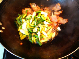 8、蒜苗炒腊肉,将蒜苗头子放入锅里，翻炒。