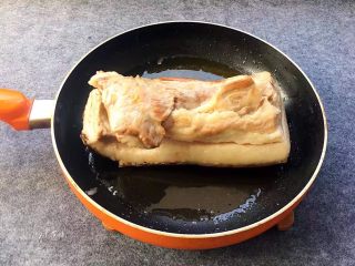 6、梅菜扣肉,锅中烧油,油温烧到六成热时,放猪肉入锅煎炸,注意煎炸的时候肉皮朝下,炸到肉皮皱起,变成金黄色后捞出,控油后待肉皮放凉回软,接着用刀切成筷子厚的长条。