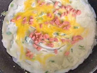 10、#懒人料理#黄金鸡蛋饼,鸡蛋摊开，撒些火腿丁。带鸡蛋快凝固时，翻面。