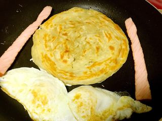 3、里脊蛋手抓饼,再次翻面，鸡蛋定型后也翻面煎熟，里脊肠也可以放在锅内一起加热。