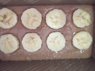 11、快手椰油巧克力酱香蕉蛋糕,倒入模具里，震一下，震平蛋糕糊，在上面放上8片香蕉