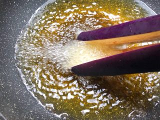 6、花样茄子,热锅放入500g油，烧至9成热，手抓茄蒂，把茄尾先放油里炸一下