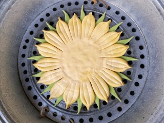 9、春暖花开,把菠菜面团做成的三角用水贴在葵花盘子造型花瓣空隙处做叶片，并放在抹了薄油的篦子上，上锅隔水大火蒸20分钟，关火后闷3分钟，出锅。
