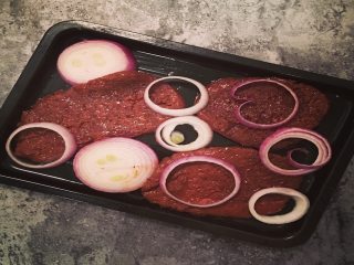 3、健身减脂杂蔬牛排,将烤箱预热，同时将腌制好的牛排放入烤盘，在牛排表面撒上洋葱圈，最后浇上耗油；