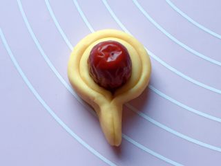 10、富贵花开枣花馍,如图：将长条对折，包住红枣，然后将两头捏紧，一个花瓣就制作完成了。（红枣提前泡发两分钟，然后清洗干净备用）