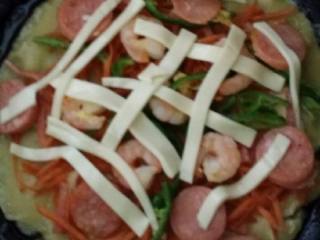 3、海鲜披萨蛋饼---睿宝私房菜,锅里放油烧开6成热。倒入面糊十秒底部以成型关火。按顺序放入培根丝胡萝卜丝葱辣椒丝。摆好火腿和虾仁。。把奶酪片切丝交叉铺均匀。。