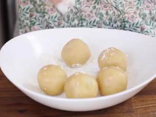 13、蛋黄莲蓉月饼,取一份饼皮面团搓圆按扁,取一份内馅放在中间,把饼皮均匀的倒扣在内馅上,反转包住内馅,在月饼表面撒面粉