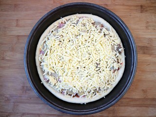 9、培根口蘑芝香披萨,最后再铺上一层芝士碎,尽可量铺满表面即可。