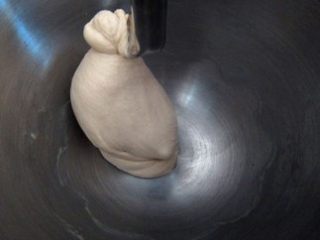 4、法式红酒金枪鱼面包,继续低速打至面团吃尽油脂，转中速打至面团表面光滑；期间可以停机一两次把面团从搅拌缸和搅拌勾上刮下来，再继续打