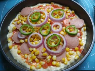 4、虾鲜拼QQ肠披萨,如图放入QQ肠和鲜虾，玉米粒，洋葱和辣椒，放入烤箱先烤15分钟