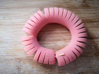 1、【童趣早餐】,先将火腿肠一切两半，接着将火腿肠放在两根筷子的中间，用刀切开，但不切断，这就是为什么用筷子的原因。整形成圆，接口处用牙签连合。