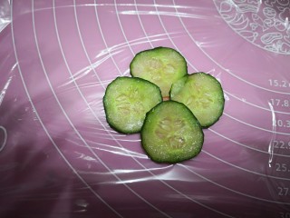 5、【童趣早餐】,开始整花型，先铺一层保鲜膜，将火腿肠切一个圆片，放中间，作为花心，接着将准备好的黄瓜片依次摆上去，作为花瓣。