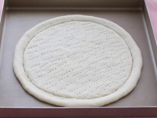 3、芝士榴莲披萨,将擀好的饼皮放进烤盘中，如果烤盘不是防粘的下面要铺上锡纸，当然也可以用披萨盘。然后用叉子在饼皮上面扎一些气孔，这样在烤制的时候就不会出现鼓包现象了。