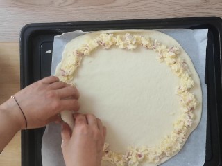 15、薯泥培根披萨,把擀好的披萨面饼放入烤盘，周围一圈放上土豆泥，然后卷起