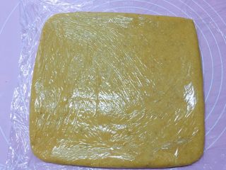 11、香酥炉果,取一张保鲜膜放在案板上,将和好的面团放在保鲜膜上,面团上再盖一层保护膜,然后用擀面杖擀成正方形。
