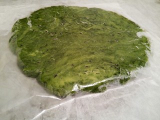 11、抹茶油酥饼干,将面团揉圆压扁，放在两张油纸中间，用擀面杖擀开，擀成大约0.5的面片（擀得要比一般的饼干厚，放在两张油纸中间擀开，面团就不会粘擀面杖和案板了）