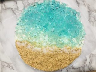 24、海洋慕斯蛋糕,在蛋糕表面分别加入酒冻，深色的先放，然后中间那里放的是浅色的，浪花可以用椰蓉装饰，我没有买到椰蓉就用白砂糖代替浪花了，然后撒上饼干碎就完成了。