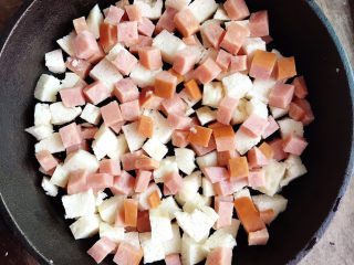 6、烤馒头披萨,铸铁锅中放入花生油，将馒头丁和火腿丁均匀的平铺在锅中