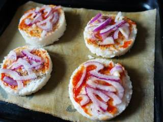 4、蛋白米饭腊肠批萨,米饭上刷番茄酱，撒黑胡椒粒，接着铺洋葱丝，然后用手捏少许盐，在洋葱上撒梅花盐