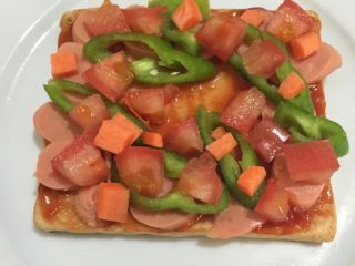 3、微波炉吐司披萨,如图放入火腿肠，青椒，西红柿，胡萝卜丁（尽量避开中间，因为接下来要放鸡蛋）