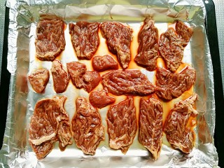 3、秘制烤牛肉披萨,将腌好的牛肉摆放在铺好锡纸的烤盘里，烤箱预热5分钟，上下火200度烤15分钟