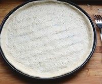 4、金枪鱼果蔬披萨,将擀好的面饼铺进 【已涂好一层薄薄黄油】的烤盘中，用手将饼皮撑至烤盘边缘，并挤出一圈圆边，用餐叉在底部扎若干排气孔。