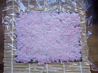 7、樱花寿司,盖上保鲜膜，用擀面杖来回擀平。