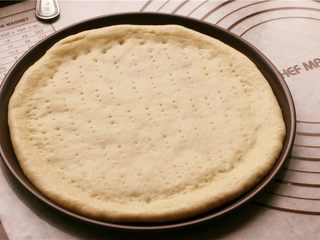 7、培根玉米粒披萨,放到披萨盘里，用叉子在面饼上扎出小孔。