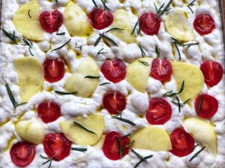 13、迷迭香佛卡夏(天然酵种),面团再次增至1倍大,二发完成。在用手指按好小坑的面团上(用手指插入面团时,能感觉到面团内部充盈的大气泡,这些大气泡另面团变得如云朵般轻盈),均匀涂抹上橄榄油,在放上土豆、小番茄和新鲜迷迭香。