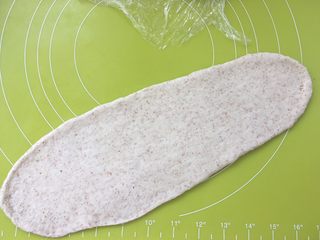11、全麦吐司,取一份松弛好的面团，用擀面杖擀成长条，松弛好的面团擀的时候有轻微回弹，回弹过大证明面团没松弛好